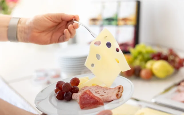 Eine Person nimmt eine Scheibe Käse vom Buffet